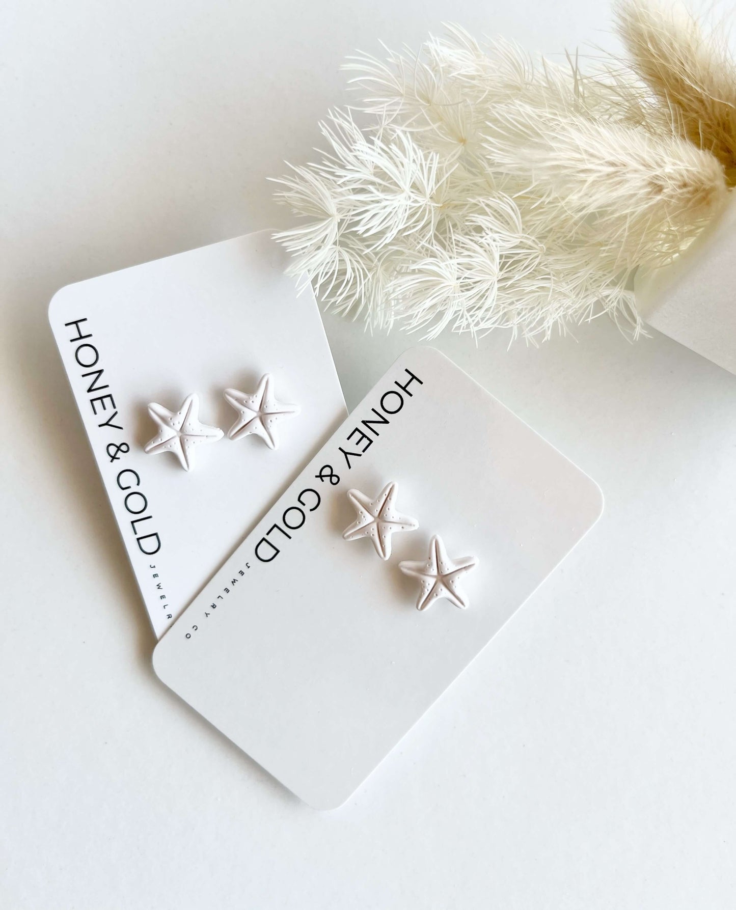 White Polymer clay starfish earrings on a branded card against a white background.