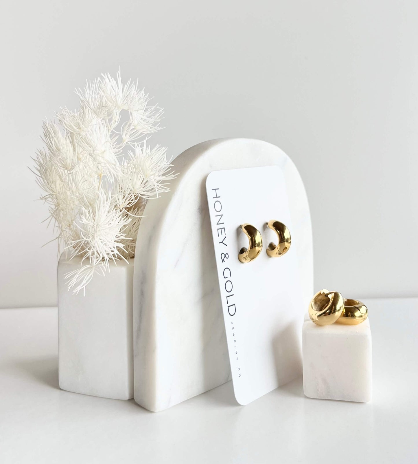 Chunky, Golden, Huggie style earrings on a white branded card. background is white with marbled accents.