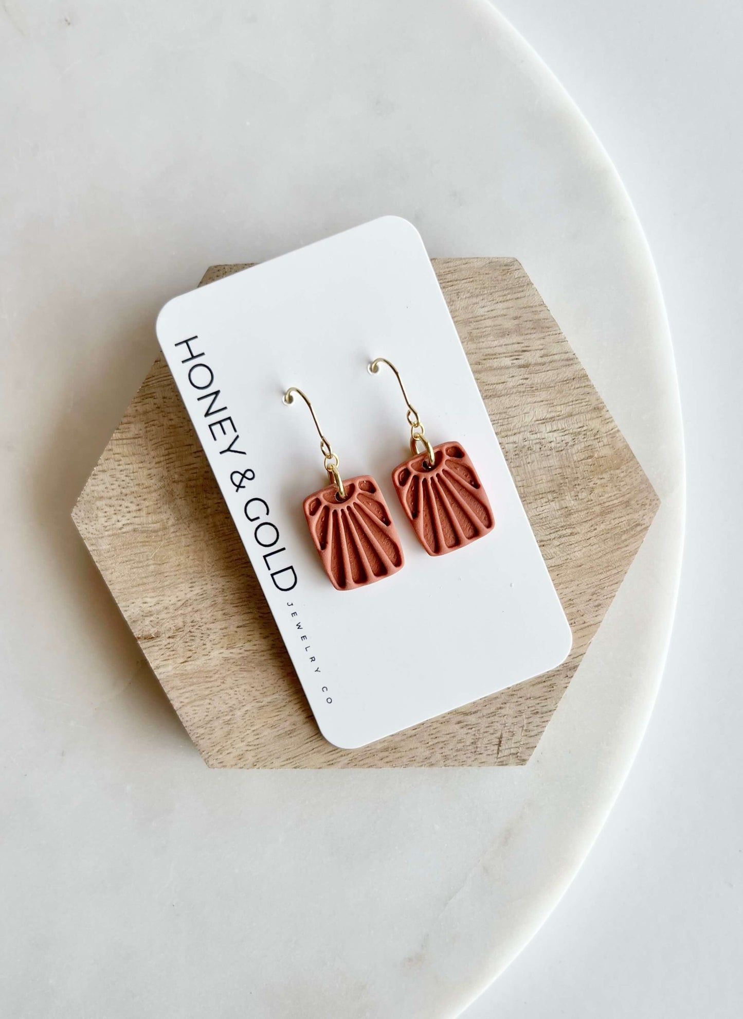 Terra Cotta Sunsetter earrings on a 'Honey & Gold' branded card with a wooden block and white plate background.