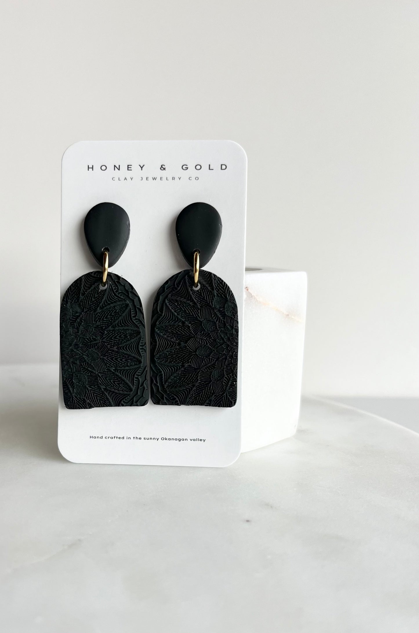 Zara in black. Drop-style earrings in a variety of velvety hues. Embellished in a mandala stamp with gold accents. 