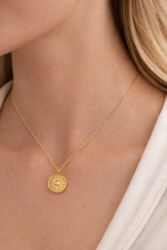 Gold necklace with a round pendant on a person wearing a white shirt.