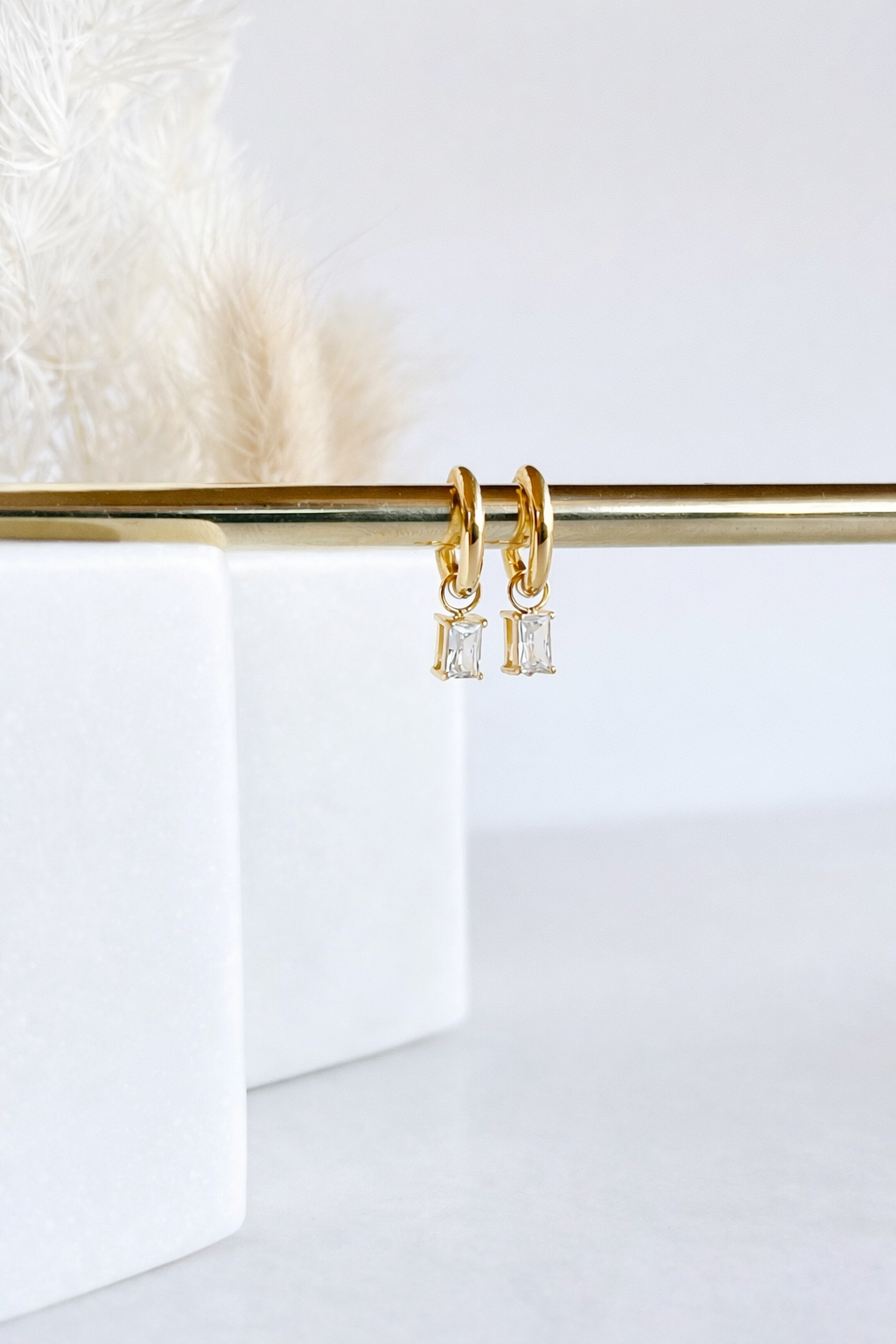 Gold hoop earrings with square-cut gemstones on a white background