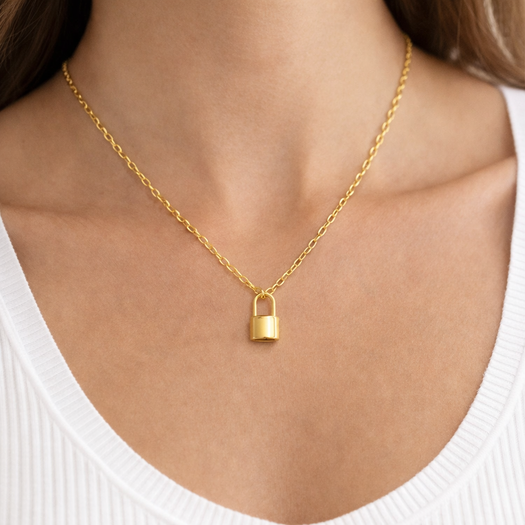 Gold Paper clip chain necklace with a lock pendant on a person wearing a white top.