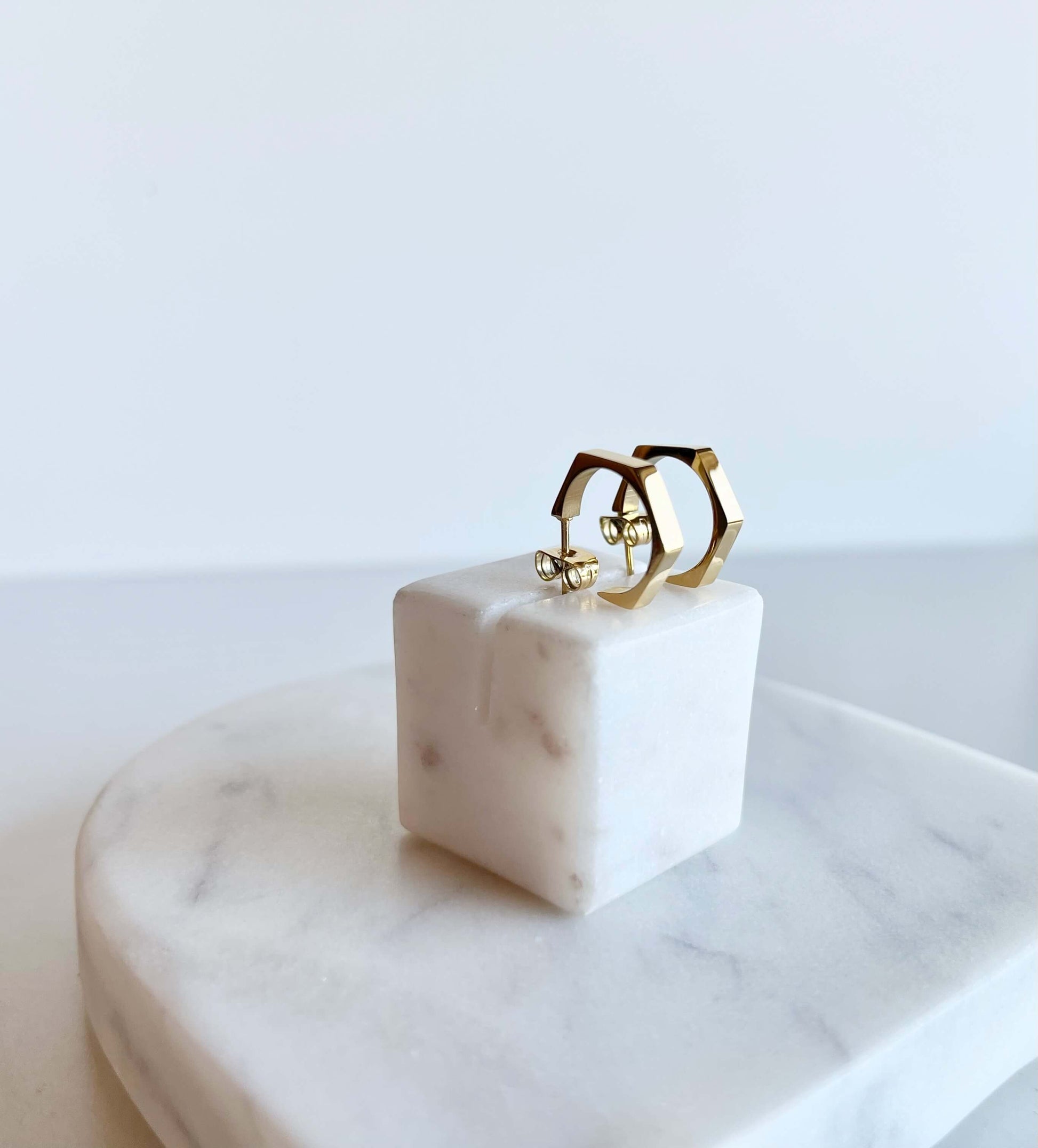 18k Gold Hexagon shaped earrings on a white marbled background