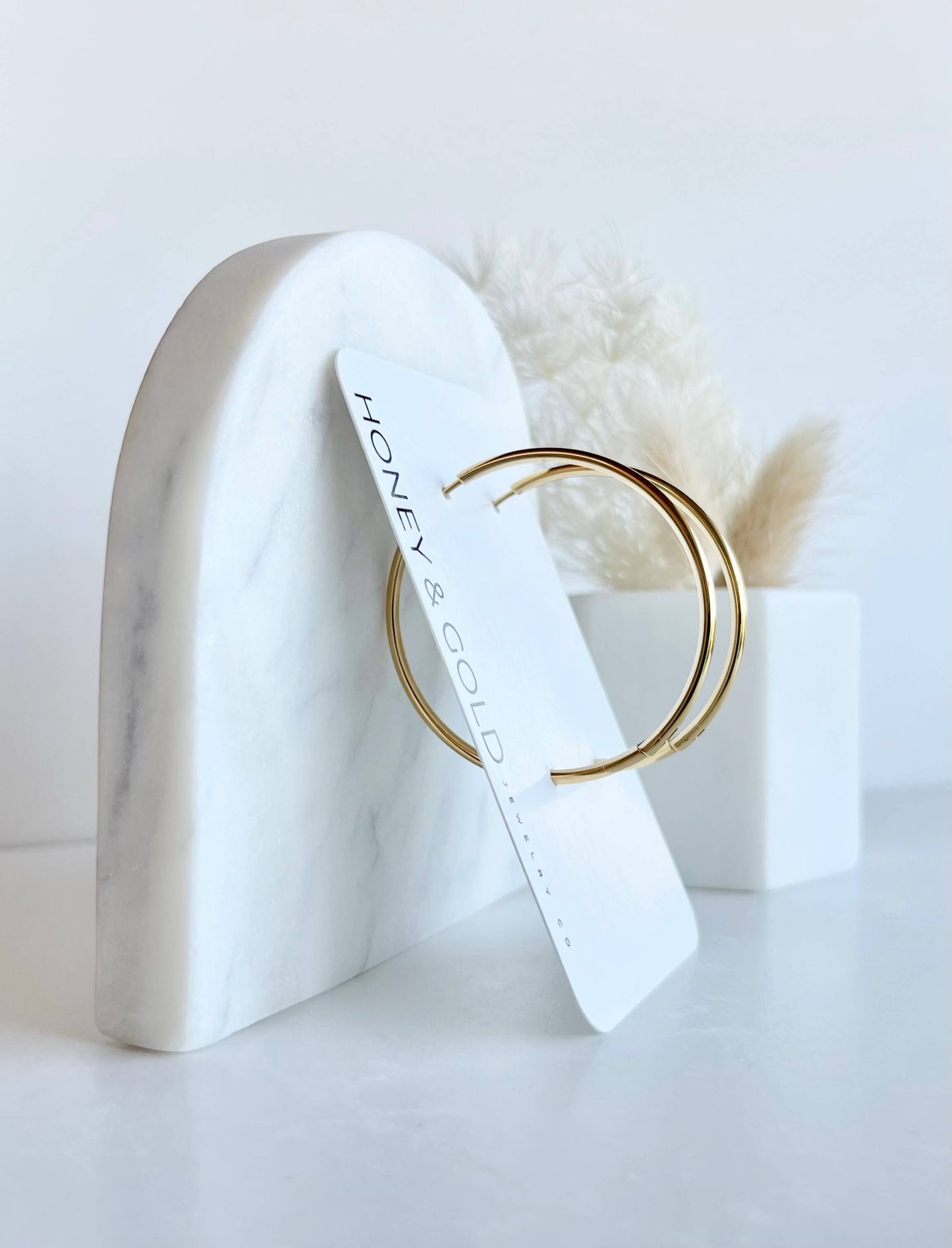 18K gold hoop earrings on a white background with soft marbled accents. Smooth, minimalist design with a 2mm thick profile.