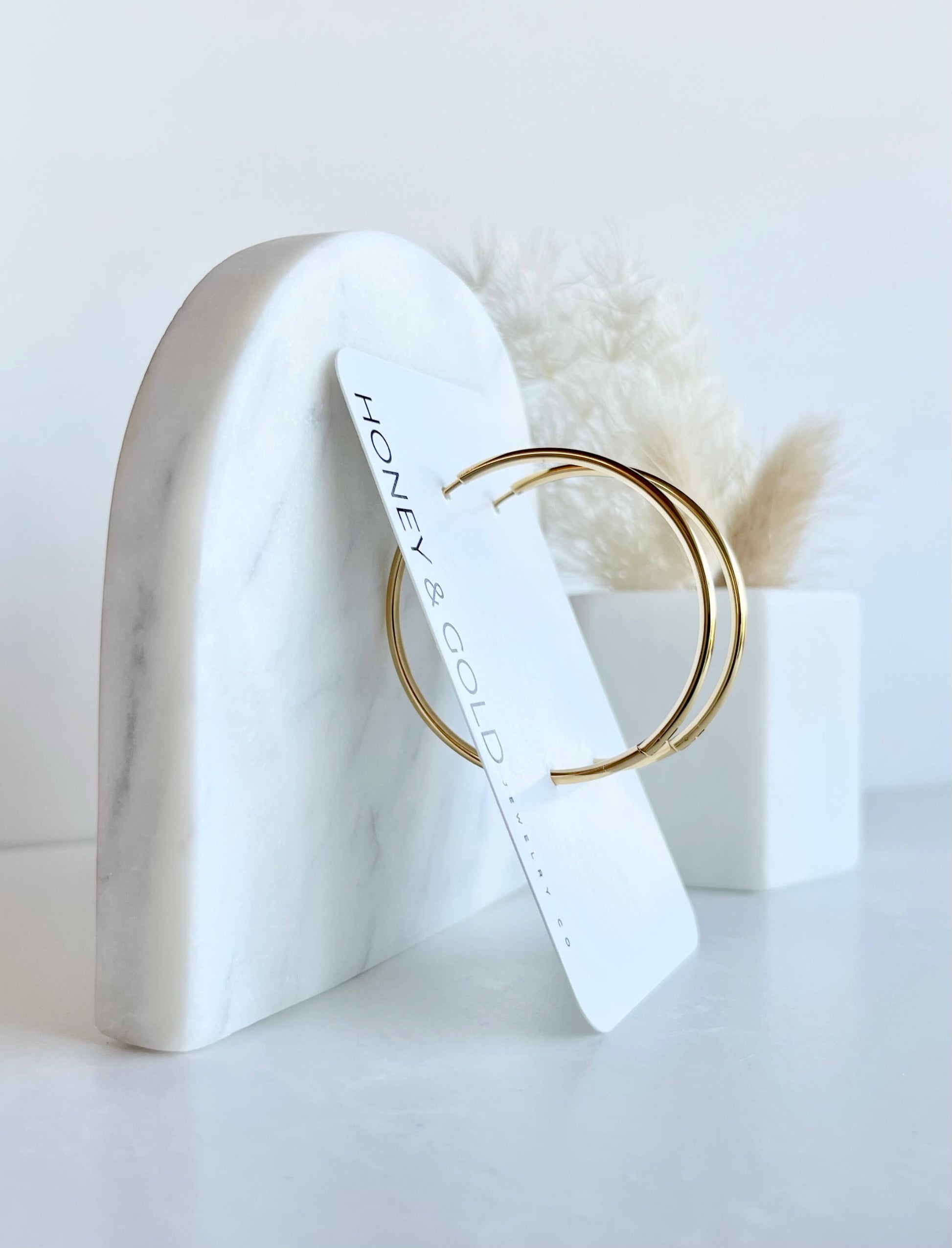 18K gold hoop earrings on a white background with soft marbled accents. Smooth, minimalist design with a 2mm thick profile.