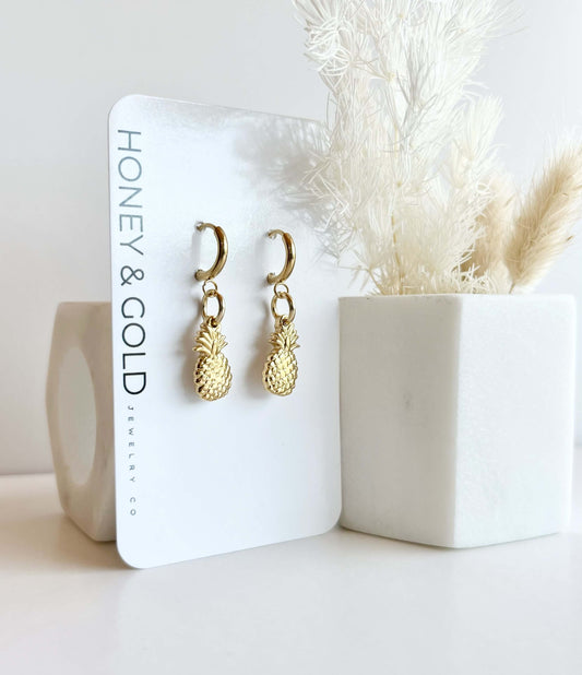 Golden stainless steel earrings with huggie toppers displayed on a branded card. background features a white backdrop with soft accents.