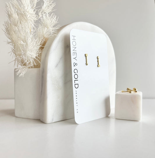Gold arrow stud earrings on a white card with modern display props, by Honey & Gold Jewelry Co
