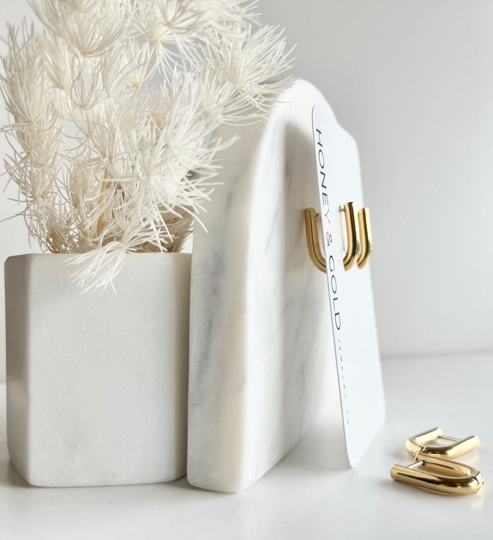 White marble display with gold huggies on branded card leaning next to a white plant on a light gray background
