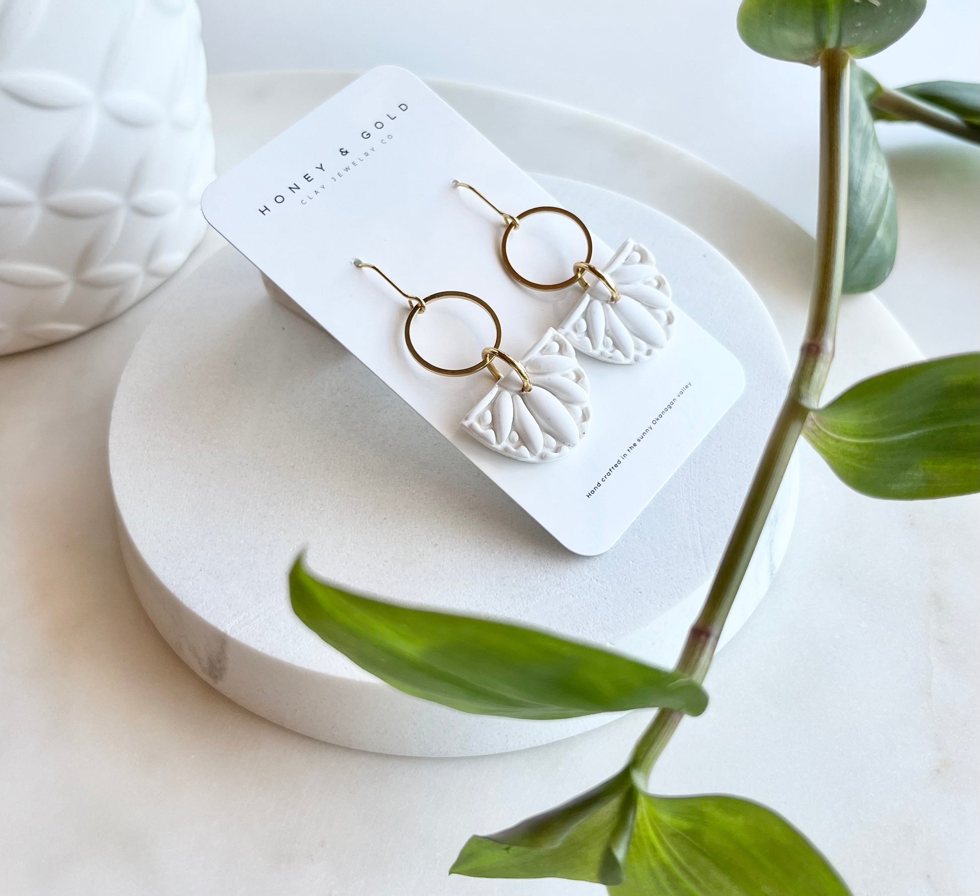 Drop Style Earrings featuring Gold accents and a white embellished clay piece suspended below. 