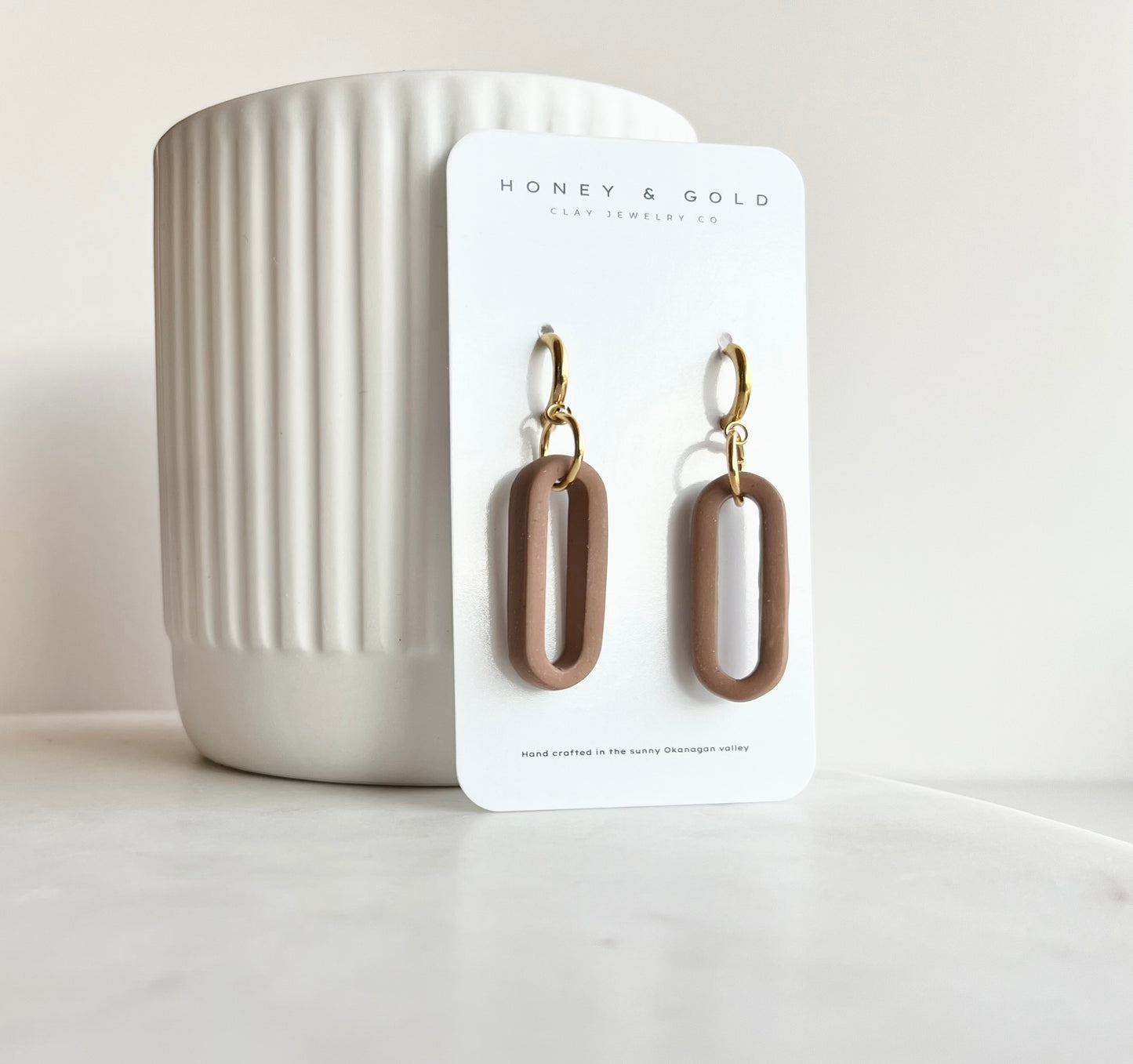 Modern earrings on a white marbled background, featuring a lightweight design with gold accents in a Sienna stone colour. The earrings have an oval shape and soft stone hues, creating an elegant and stylish appearance."