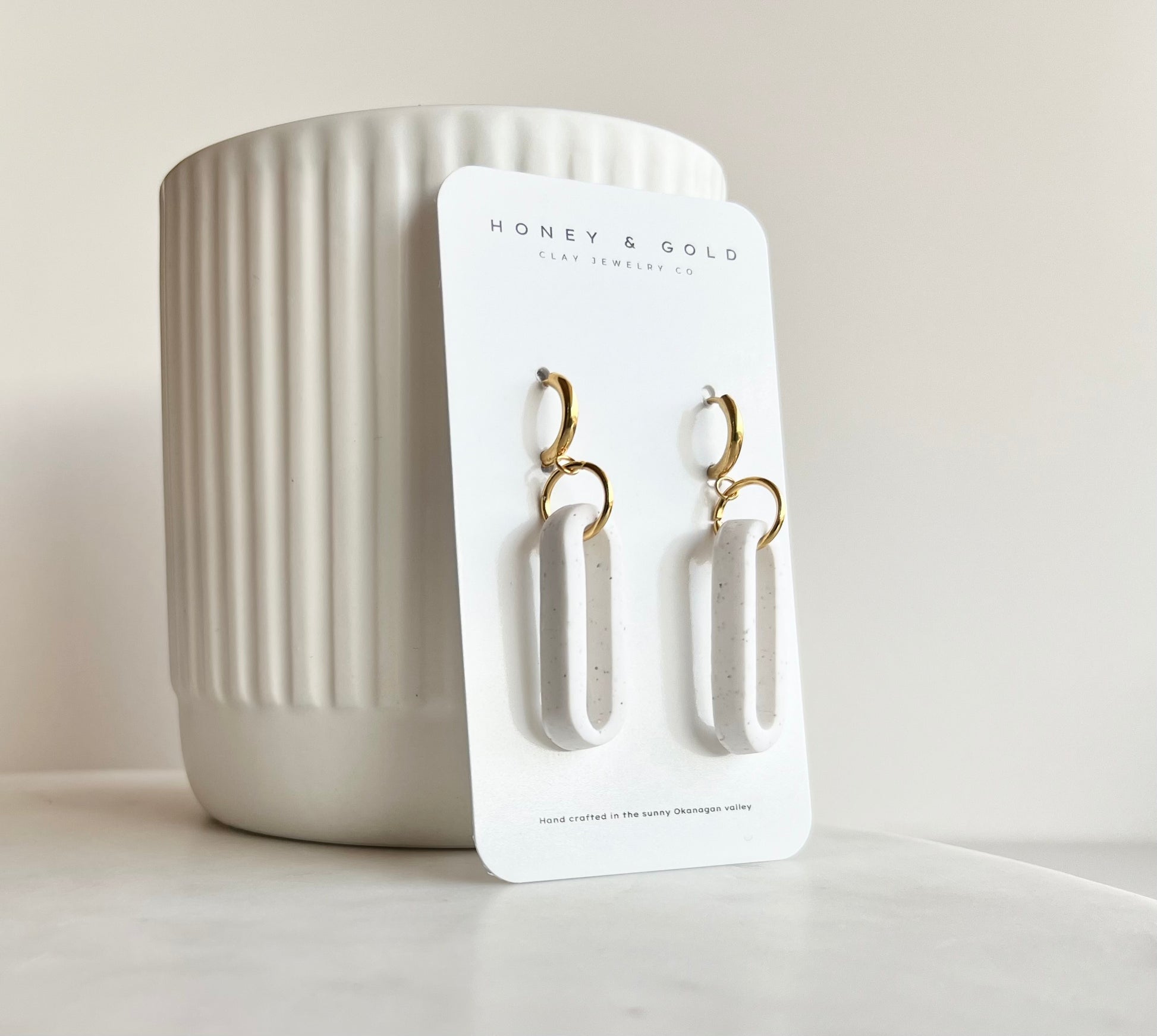 Modern earrings on a white marbled background, featuring a lightweight white design with gold accents. The earrings have an oval shape and soft stone hues, creating an elegant and stylish appearance."