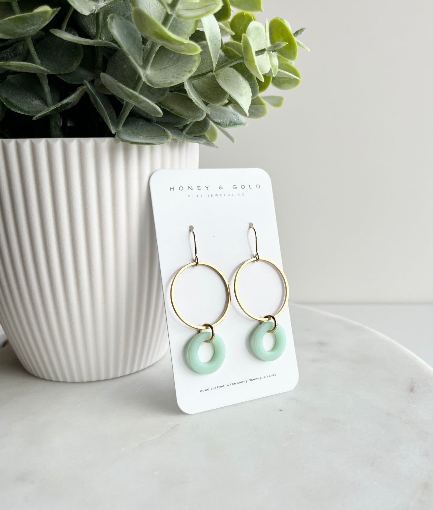 Close-up of Kai earrings featuring a delicate French hook topper with a circular golden hoop and a faux sea glass accent in teal. The earrings exude beach-inspired boho vibes, perfect for adding a subtle pop of color to any summer outfit."